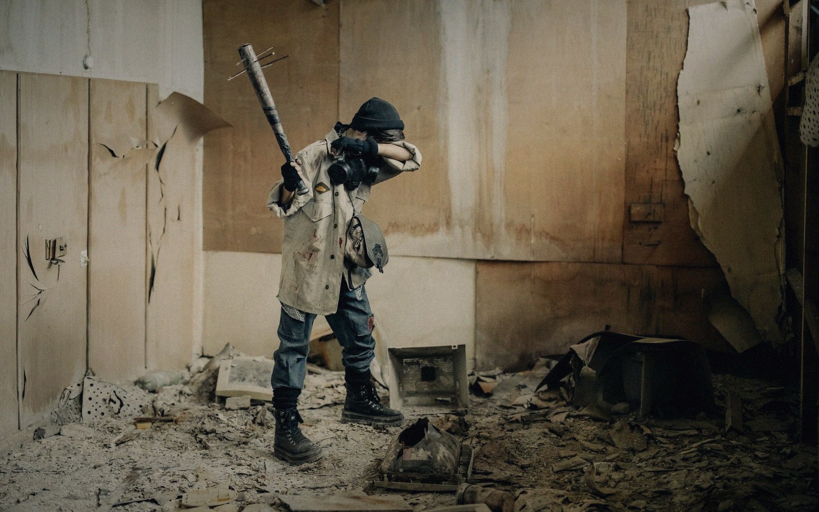 A masked figure wields a nail-studded bat inside a debris-strewn, decaying room