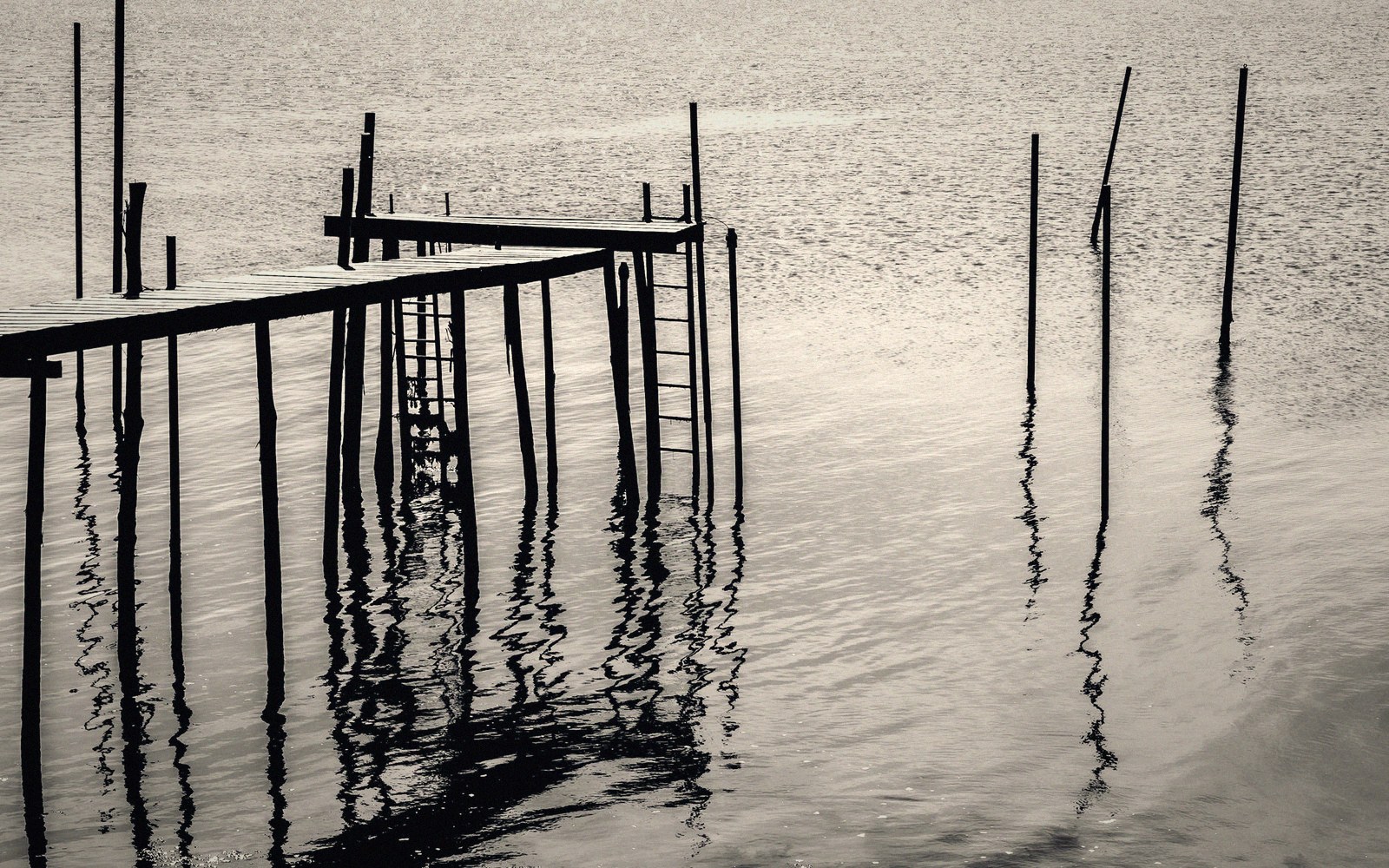 Wooden stilt pier with ladder and mooring poles reflected in still water