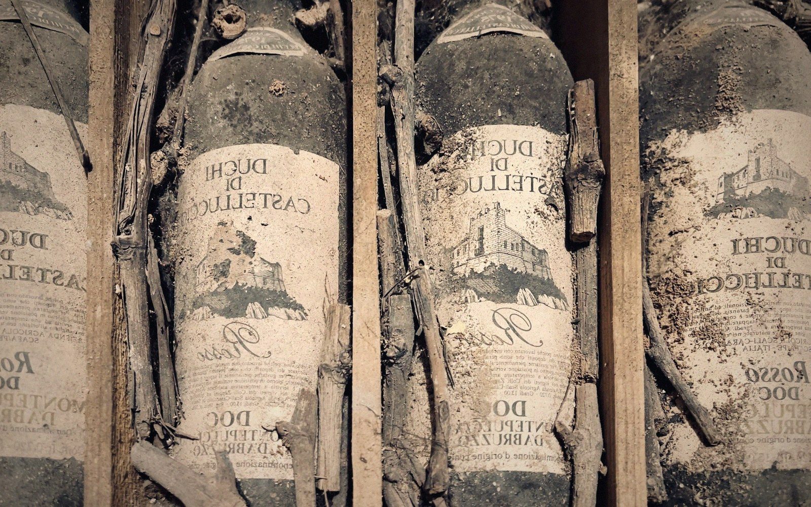 Dusty wine bottles labeled Duchi di Castelluccio lie stacked in a wooden crate